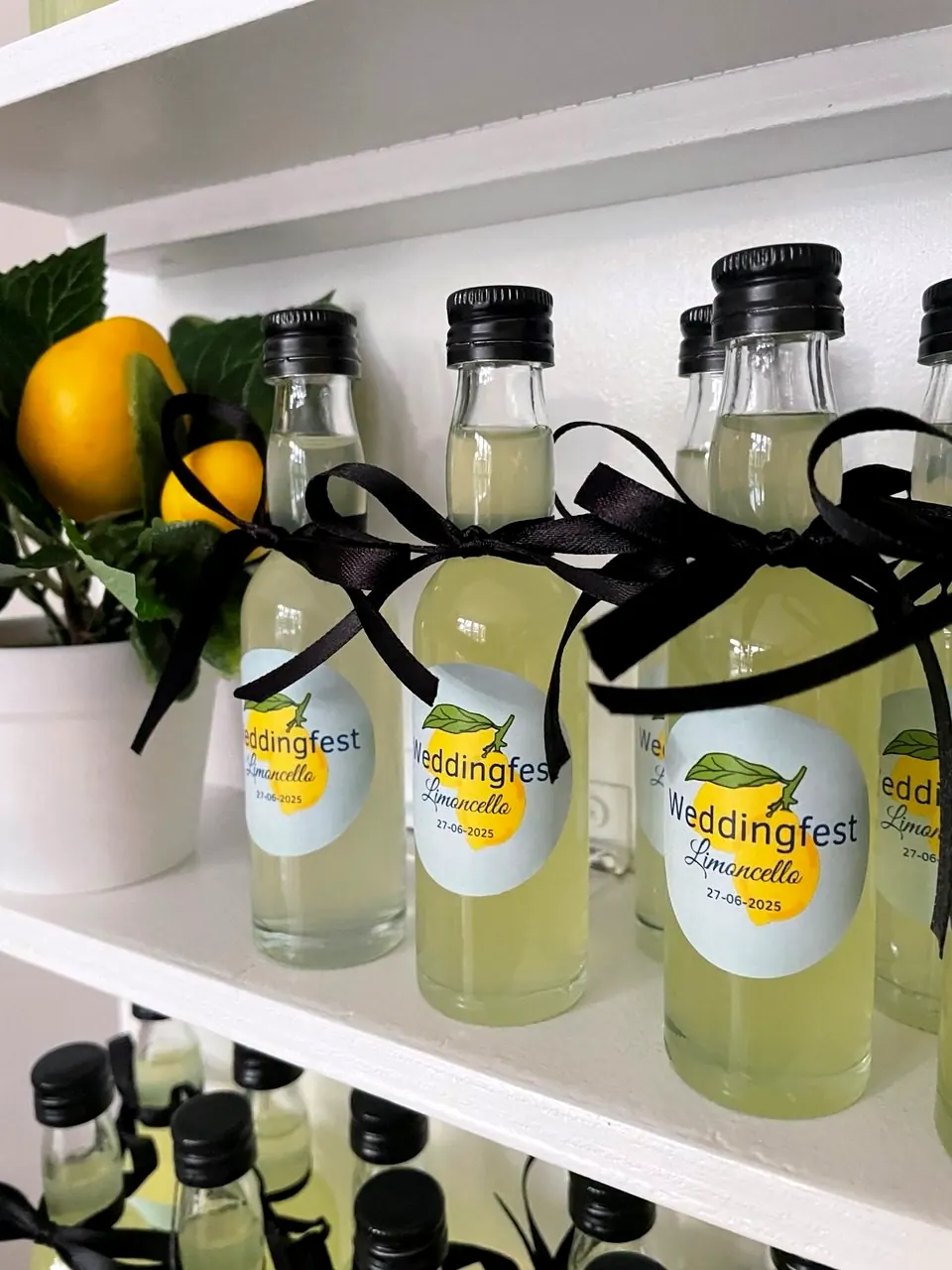 Mini-flesjes limoncello met gepersonaliseerde Weddingfest-etiketten en zwarte strikjes